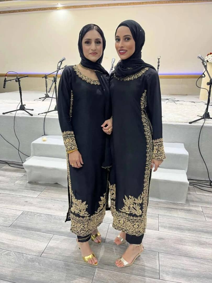 Two women wearing elegant black qameez with gold embroidery, showcasing traditional attire perfect for formal occasions.