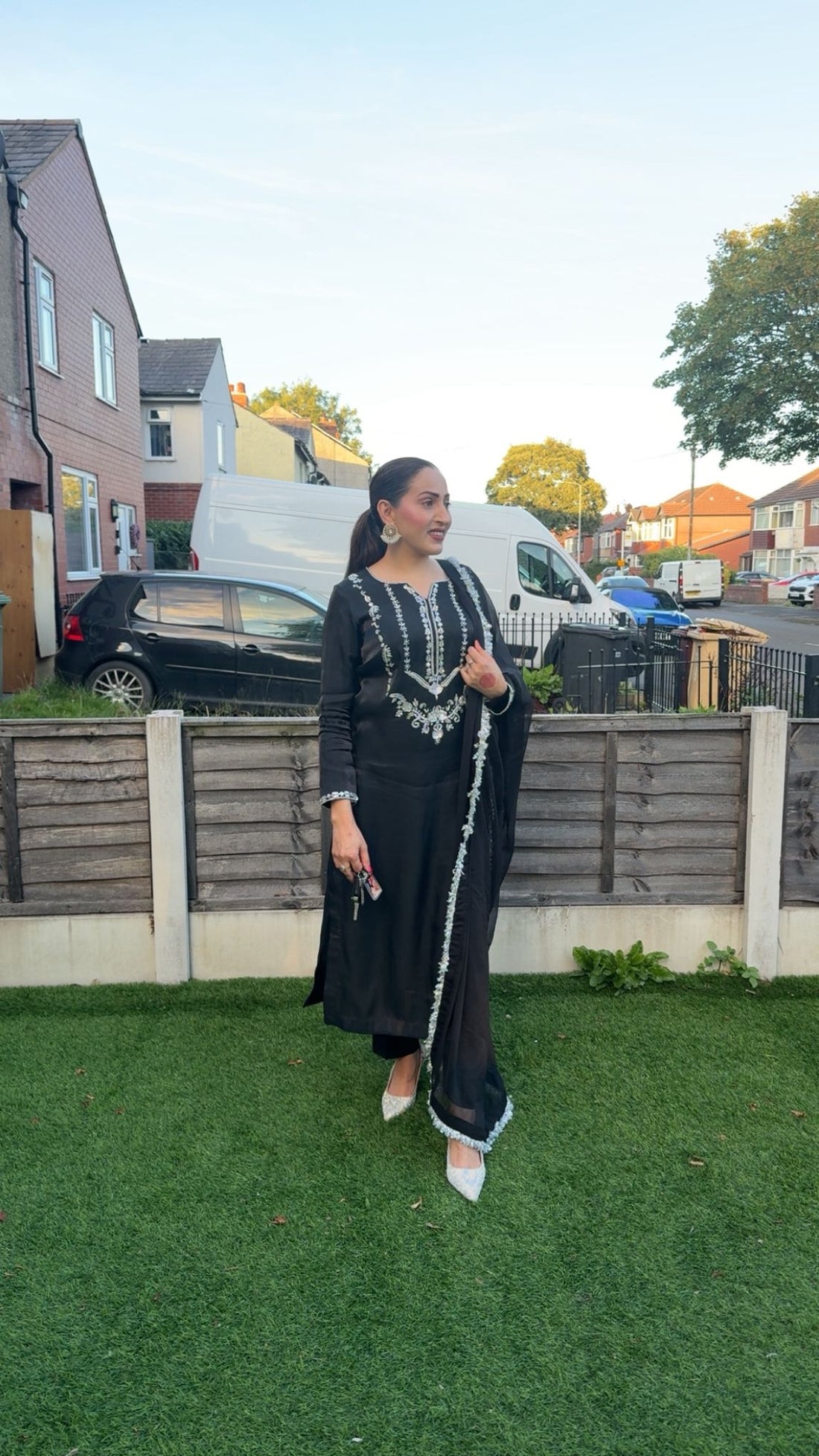 Woman in black embroidered shisha silk dress, standing outdoors, showcasing traditional elegance and style.